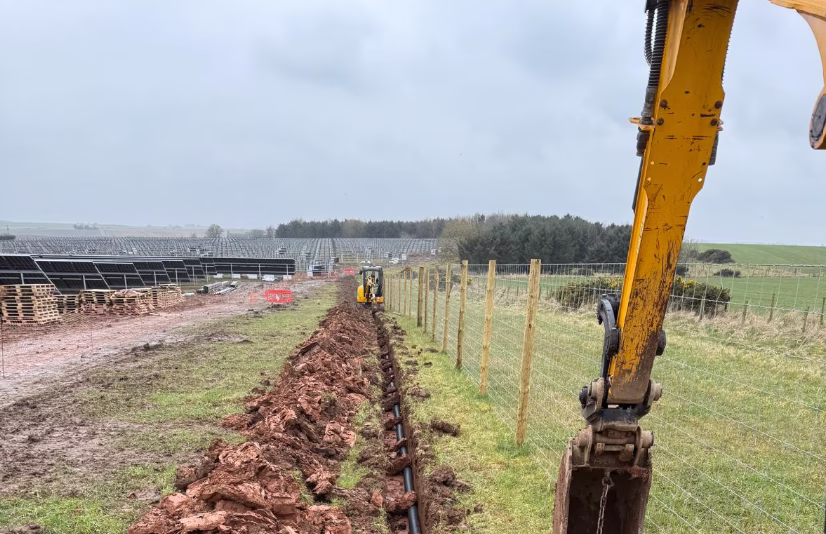Civils machinery digging trenches on a solar farm site to lay CCTV for renewable energy security